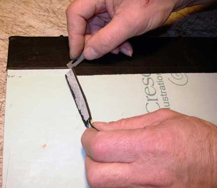 Trimming excess leather from book cover with a razor blade.